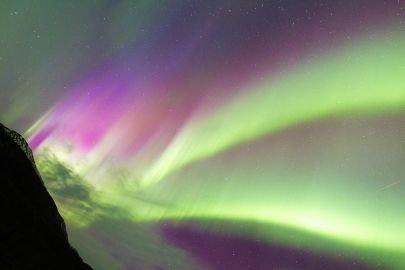 The northern lights spill out from behind a mountain on a guided tour.